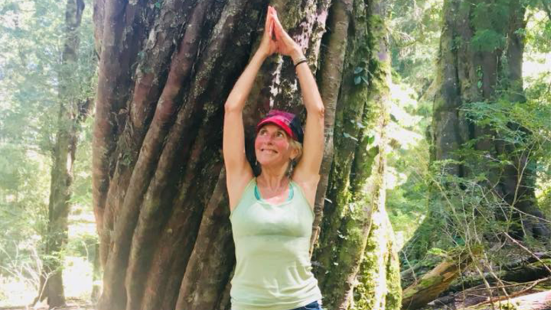Shirley McClelland is picture in a yoga pose in front of a tree.